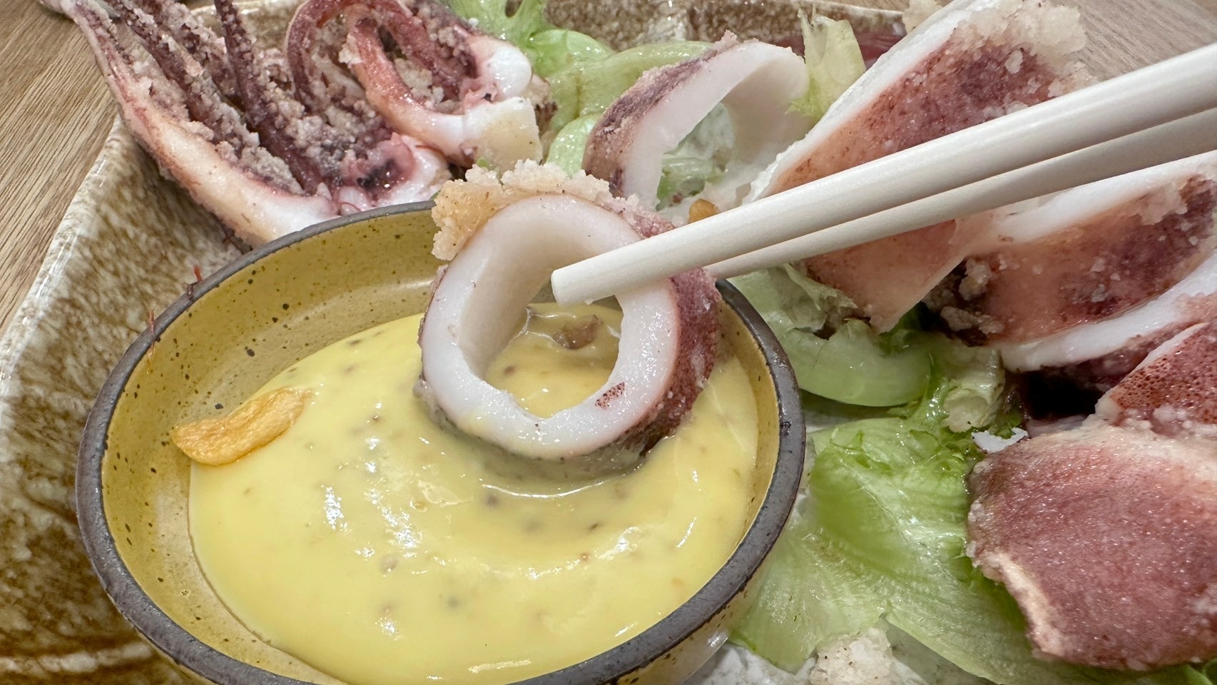 筷子夾起魷魚圈沾蜂蜜芥末醬