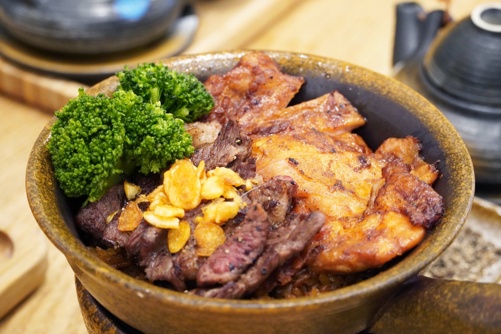 豪華雙拼釜飯上的牛小排、烤雞腿排、蒜片與花椰菜